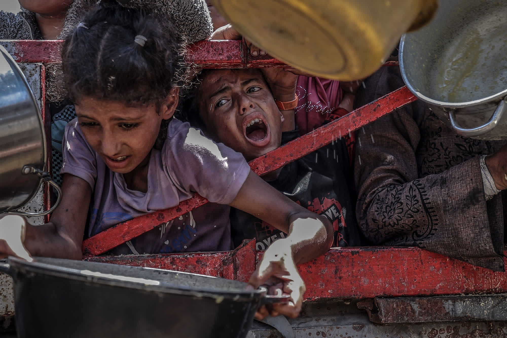 Children in Gaza crying and reaching desperately for food at a distribution point